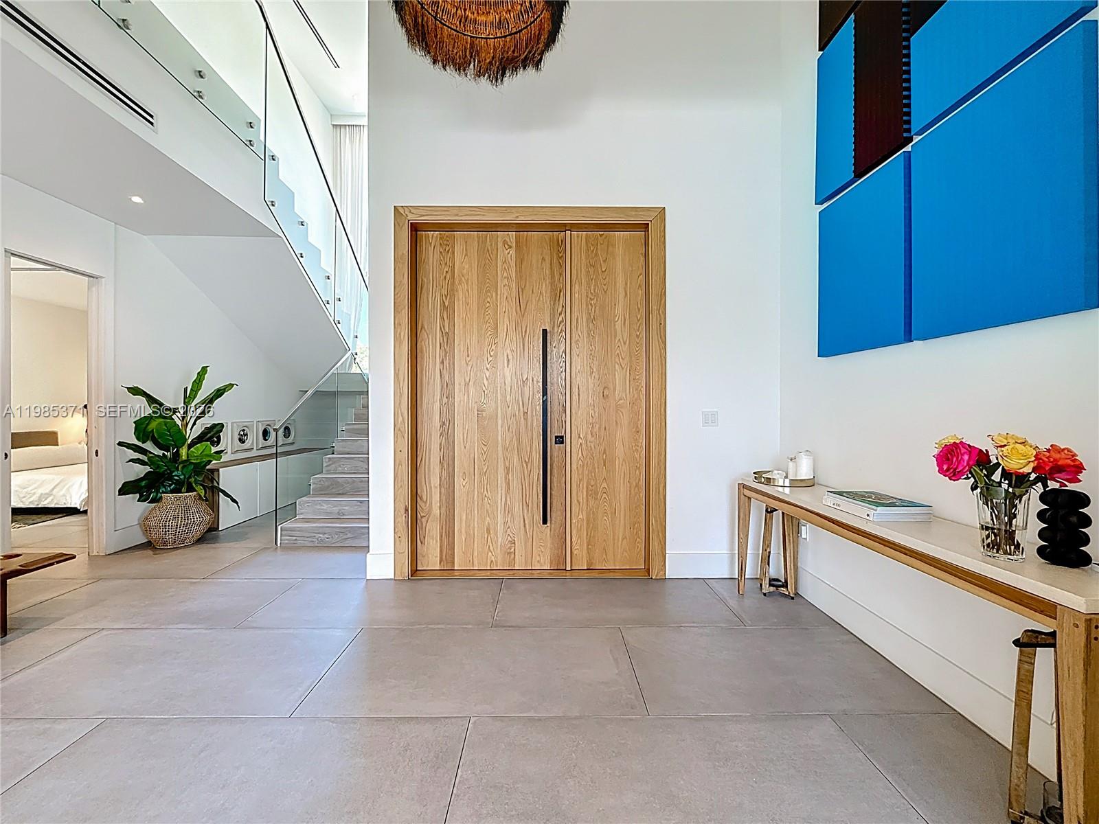 A modern entryway features large light wood double doors, a glass-railed staircase, and tile flooring — 561 Warren Ln, Key Biscayne FL 33149, KEY BISCAYNE, FL