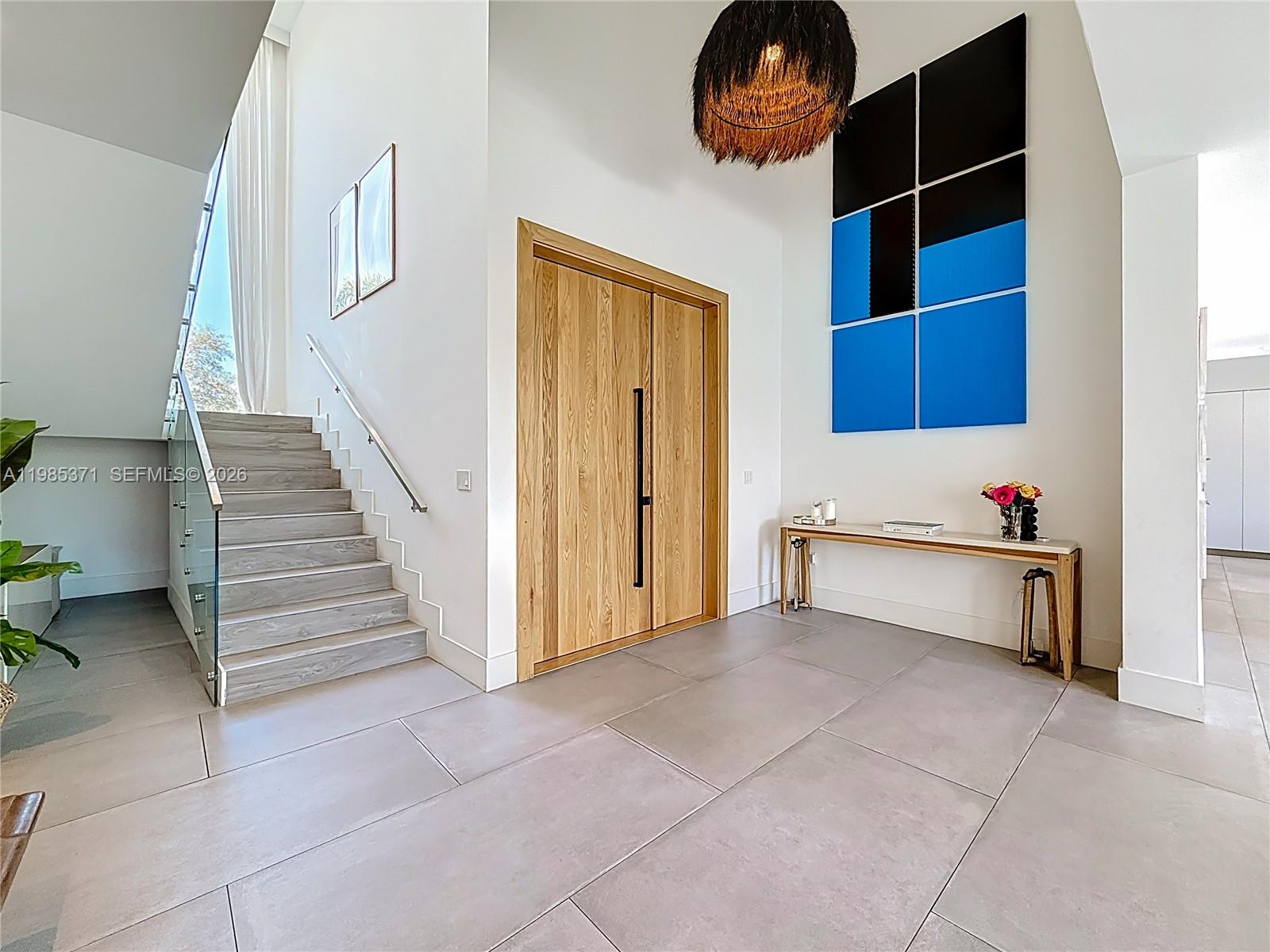 A modern foyer features large tile flooring, a wooden double door, and a floating staircase — 561 Warren Ln, Key Biscayne FL 33149, KEY BISCAYNE, FL