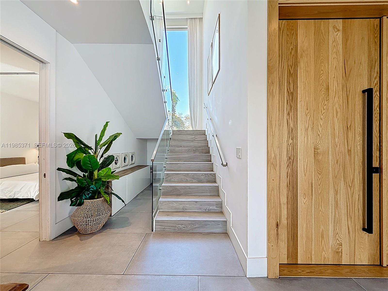 A modern interior features a wooden door, a staircase with glass railings, and a potted plant — 561 Warren Ln, Key Biscayne FL 33149, KEY BISCAYNE, FL