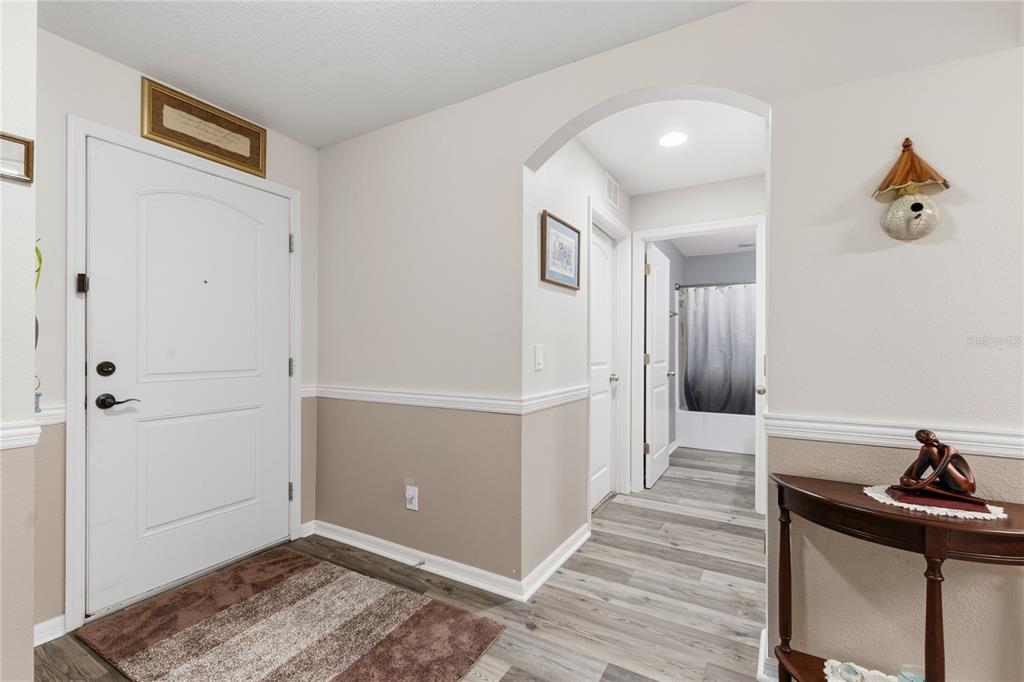 An entryway features a white front door, light-colored walls with wainscoting, and wood-look flooring — 5581 MAGGIORE BOULEVARD, LAKELAND, FL