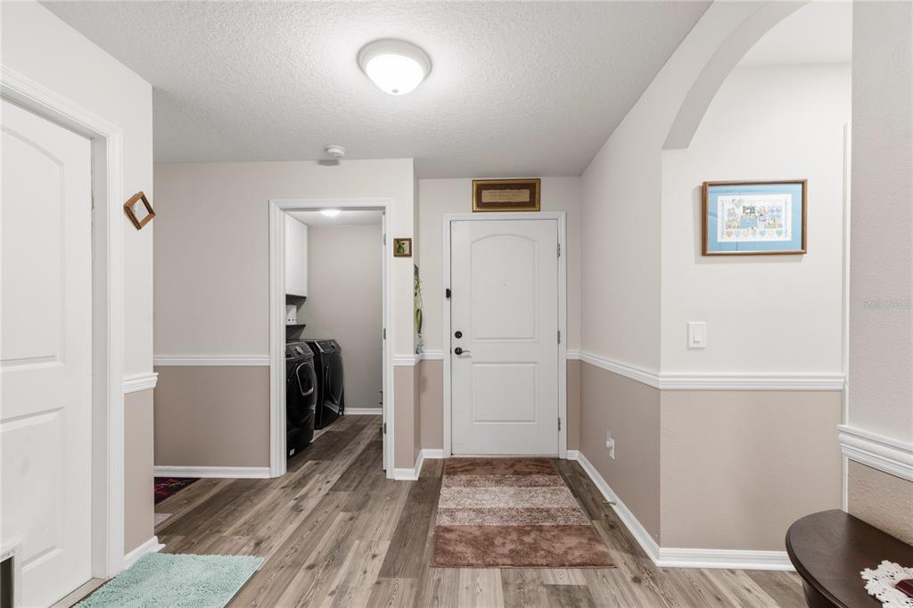 An entryway with wood-look flooring, a white front door, and a doorway to a laundry room — 5581 MAGGIORE BOULEVARD, LAKELAND, FL