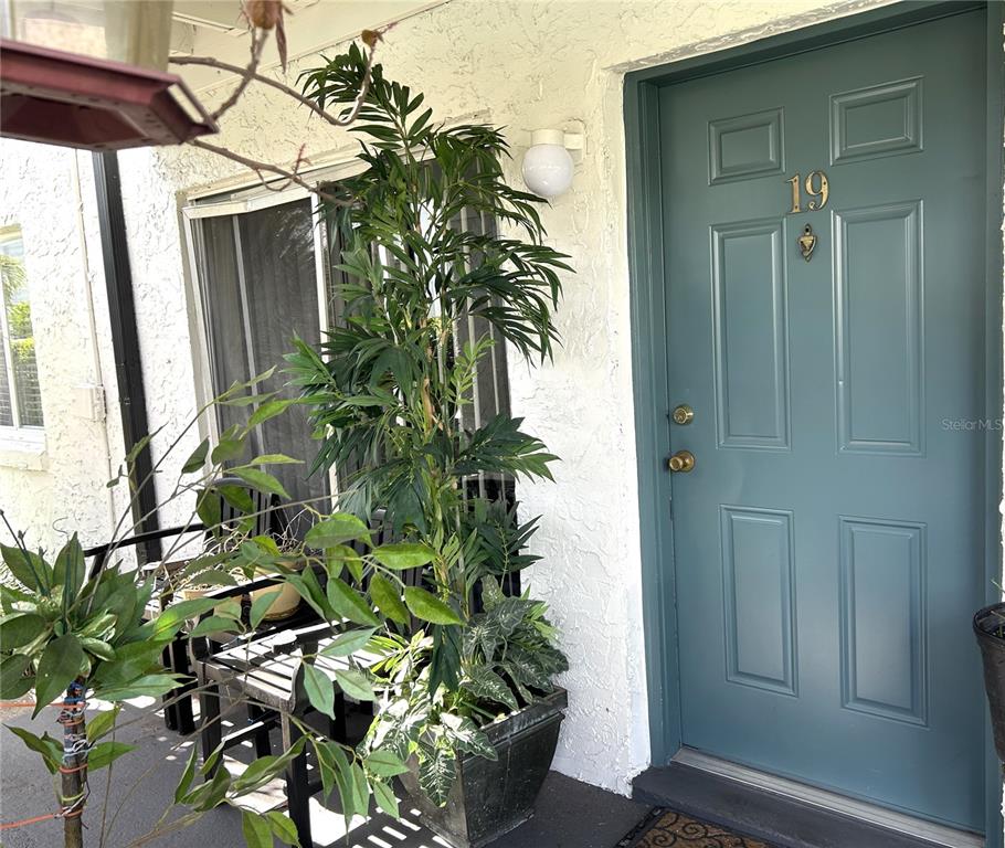 A teal front door with the number 19 sits beside a potted plant and bench — 4115 S SEMORAN BOULEVARD UNIT 19, ORLANDO, FL