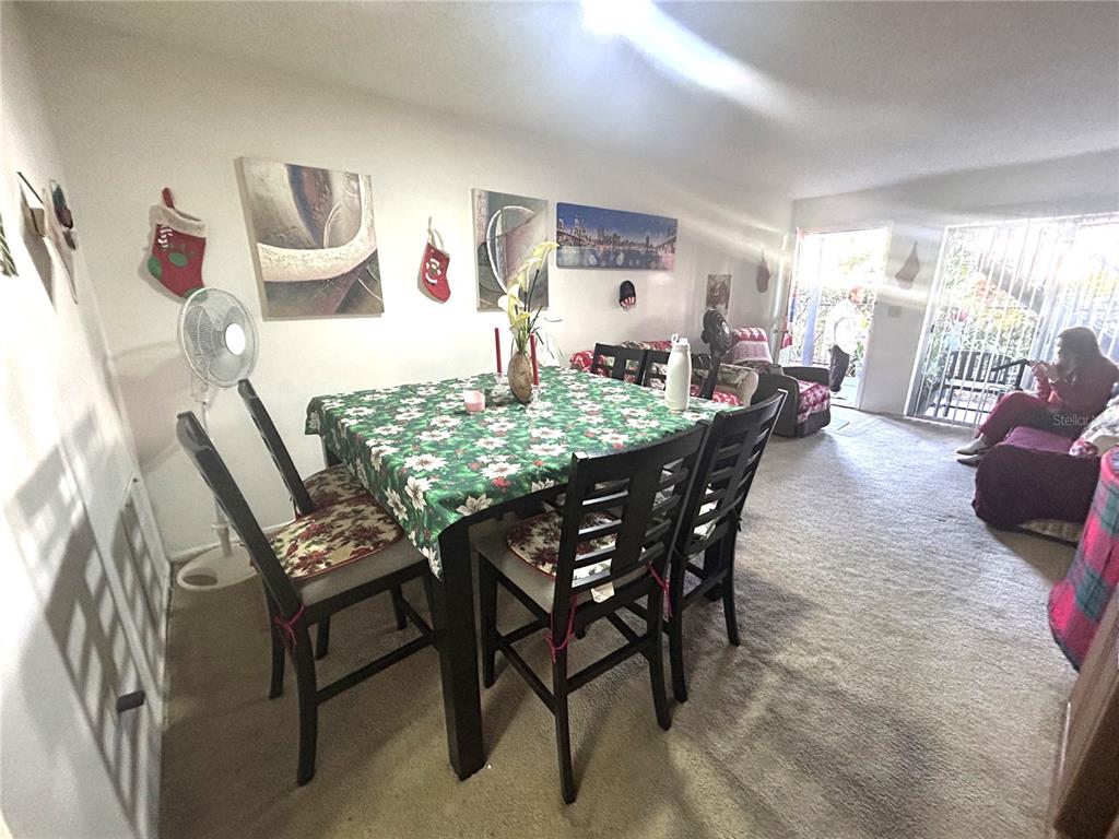A dining area with a floral tablecloth, dark chairs, and wall art leads to a living space — 4115 S SEMORAN BOULEVARD UNIT 19, ORLANDO, FL