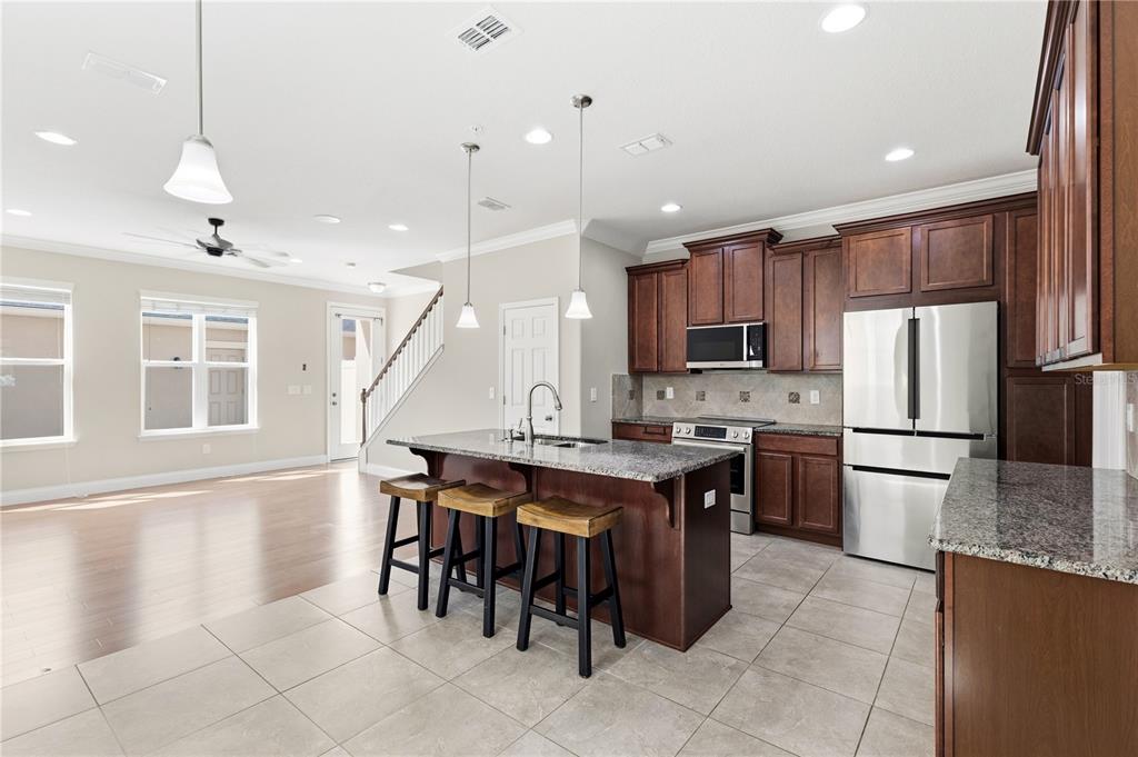 A kitchen with dark wood cabinets, granite countertops, and an island with three bar stools — 8049 CADMAN STREET, ORLANDO, FL