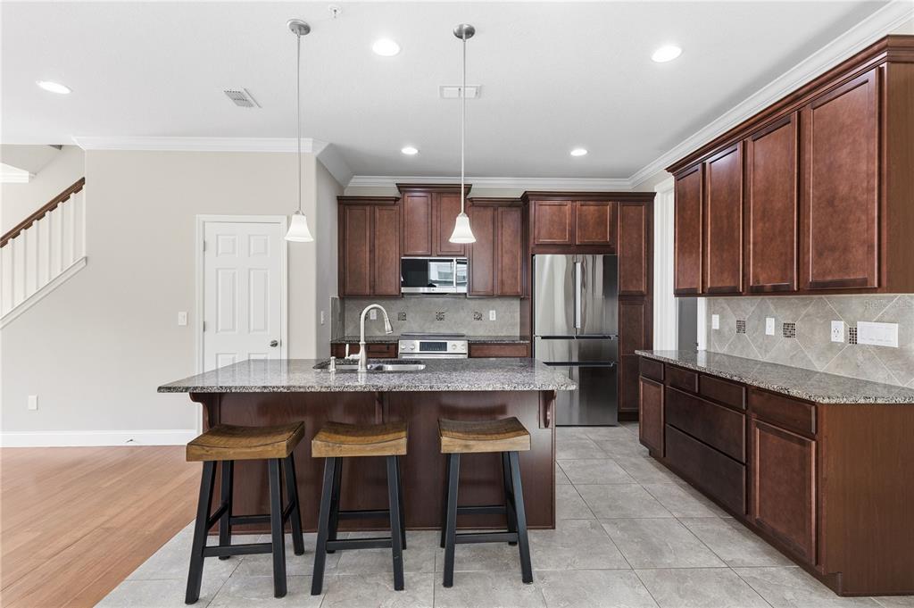 A kitchen features dark wood cabinets, granite countertops, a center island with stools, and stainless appliances — 8049 CADMAN STREET, ORLANDO, FL