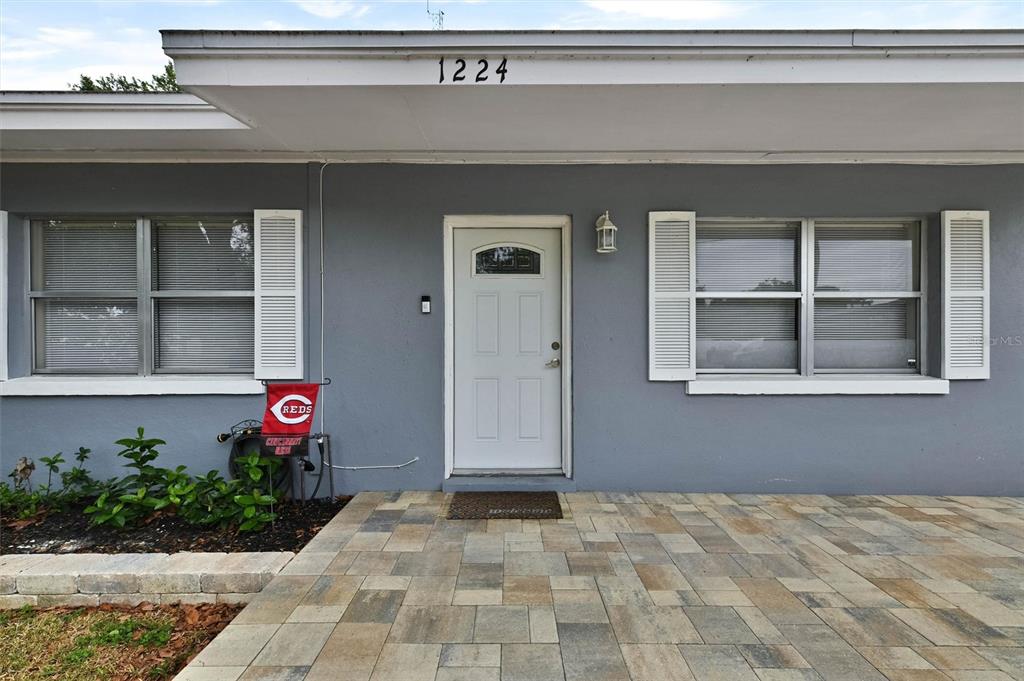 The exterior of a gray house features a paved patio, white door, and two windows — 1224 BELLEVUE BOULEVARD, CLEARWATER, FL