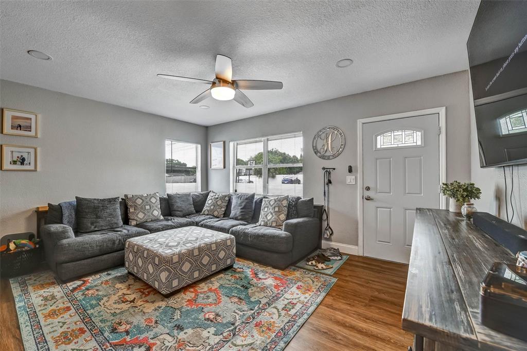A living room features a gray sectional sofa, patterned ottoman, area rug, and front door — 1224 BELLEVUE BOULEVARD, CLEARWATER, FL