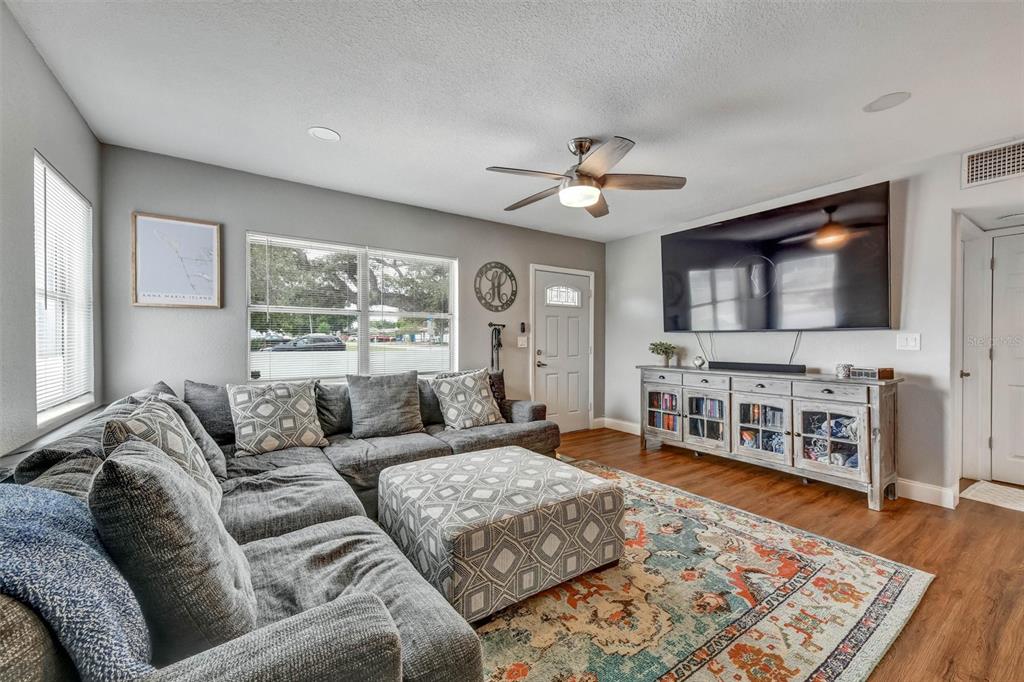 A living room features a gray sectional sofa, a patterned ottoman, and a wall-mounted television — 1224 BELLEVUE BOULEVARD, CLEARWATER, FL