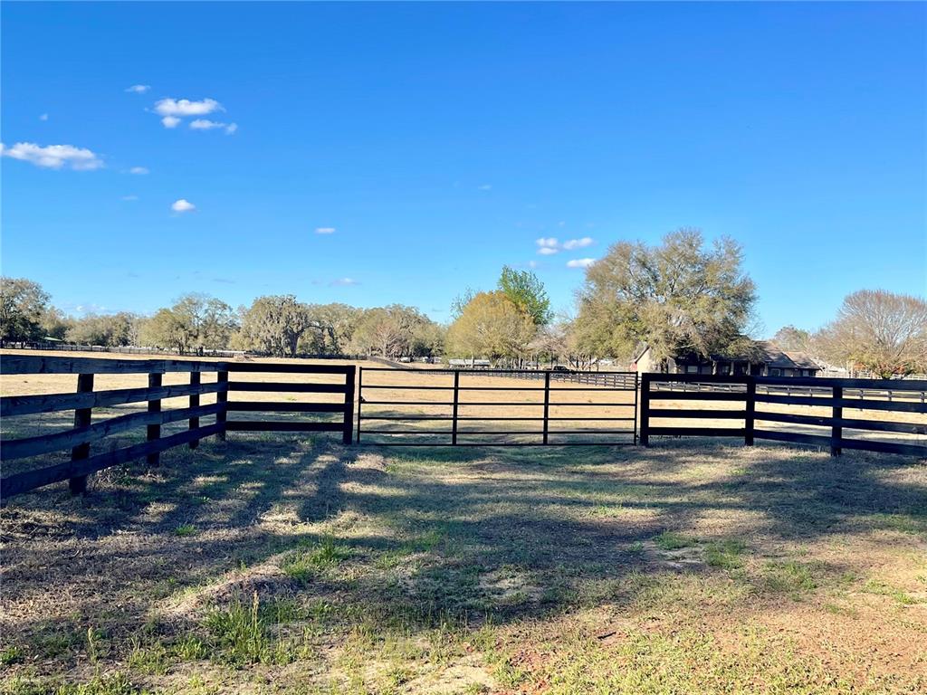 A black metal gate stands between wooden fence sections in a grassy field — 15153 SE 73RD AVENUE, SUMMERFIELD, FL