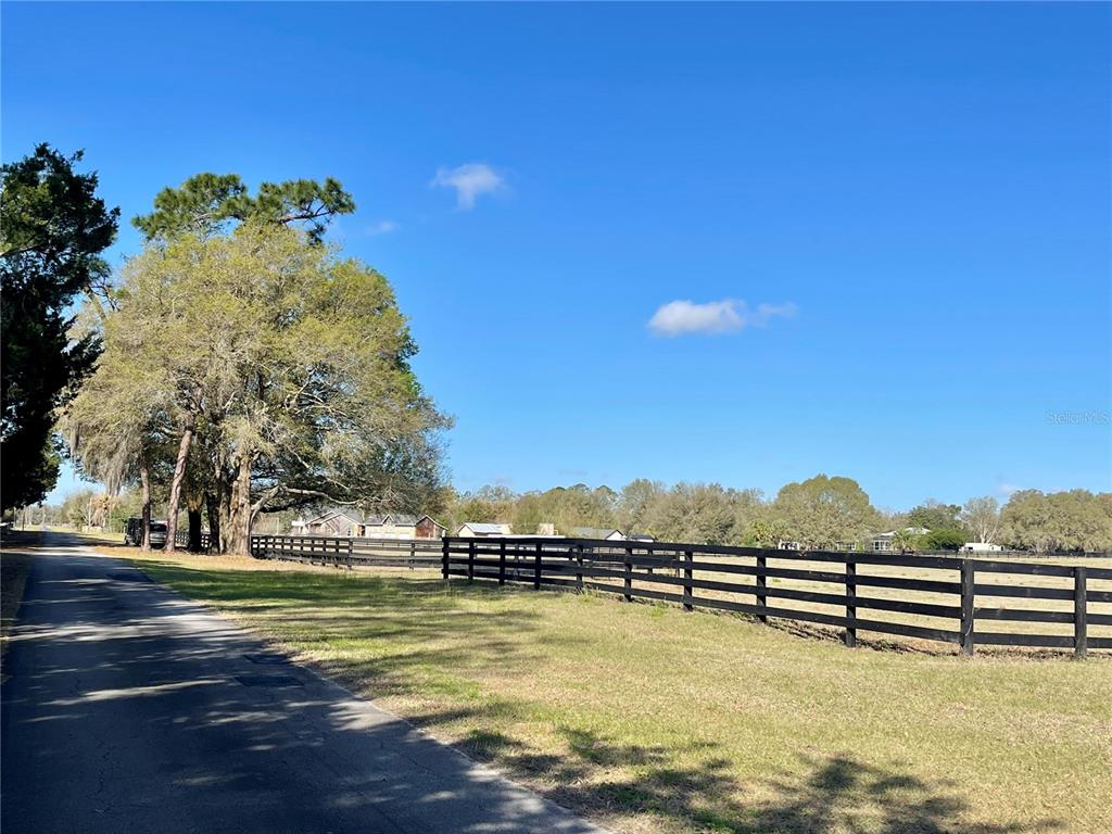 A paved road runs alongside a grassy field enclosed by a black wooden fence — 15153 SE 73RD AVENUE, SUMMERFIELD, FL