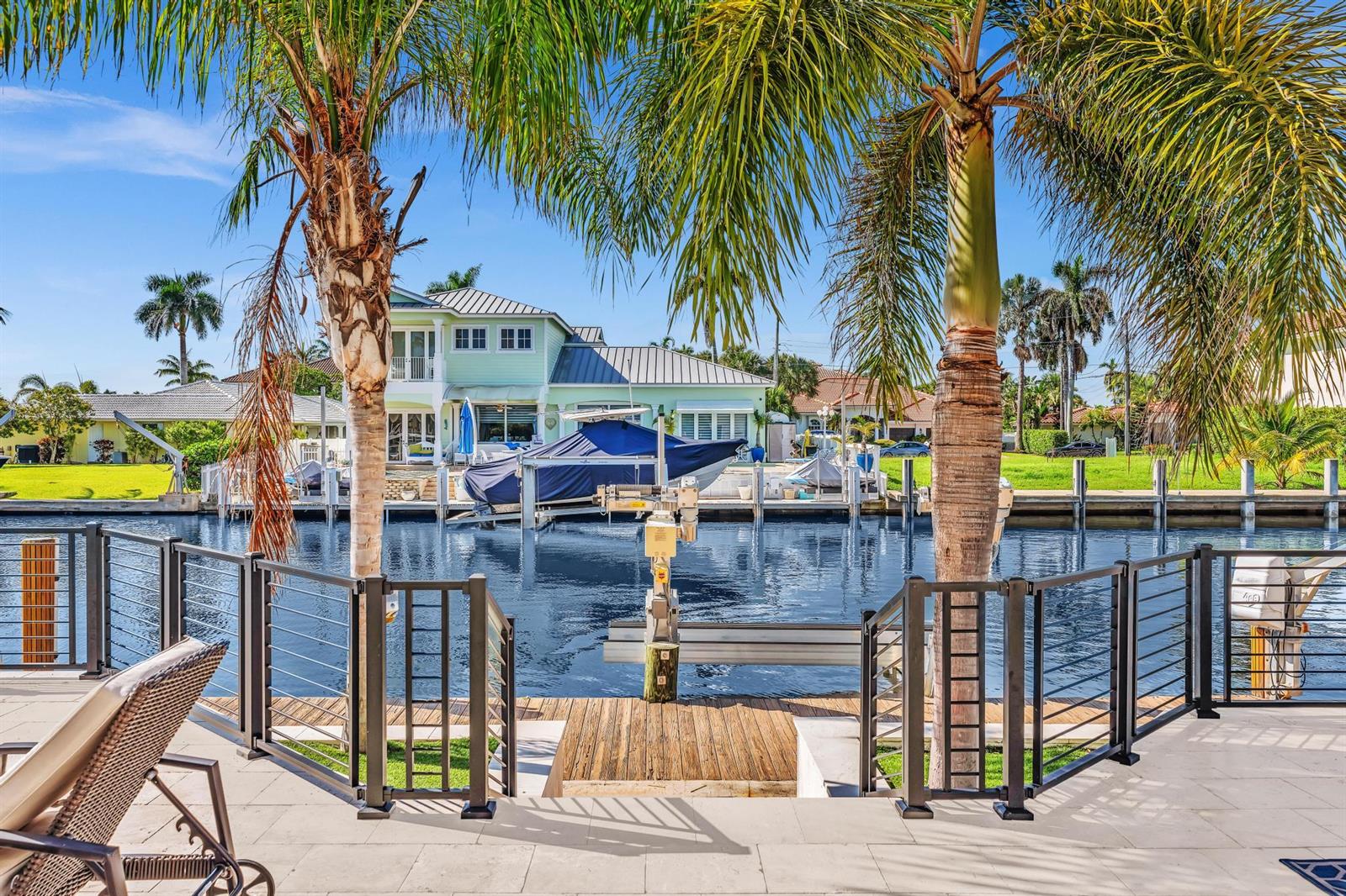A view from a patio overlooking a canal with a boat lift and palm trees — 2888 NE 33rd Street, Lighthouse Point FL 33064, LIGHTHOUSE POINT, FL