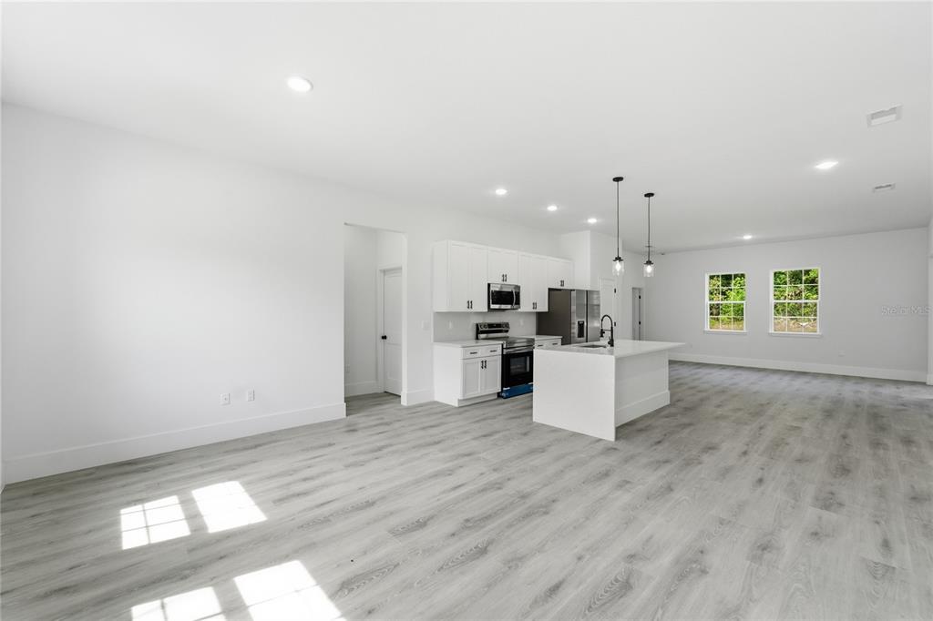 An open-concept kitchen features white cabinetry, a central island, and light wood-look flooring — 238 E CALDWELL DRIVE, DUNNELLON, FL