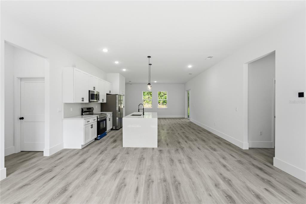 A modern kitchen features white cabinets, a central island, and light wood-look flooring — 238 E CALDWELL DRIVE, DUNNELLON, FL