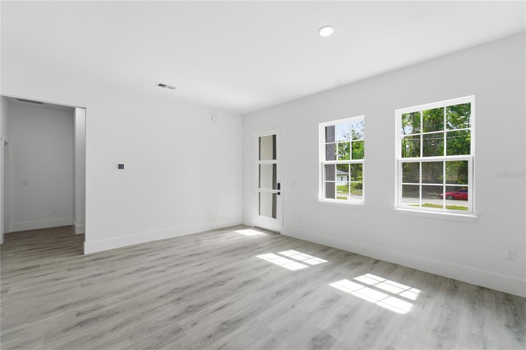 A bright, empty room features light wood-look flooring, white walls, two windows, and a door — 238 E CALDWELL DRIVE, DUNNELLON, FL