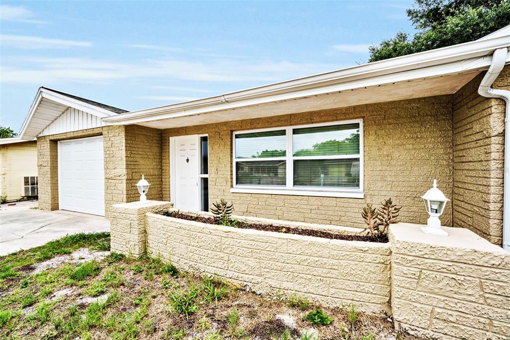 A tan brick house exterior features a white front door and a raised planter bed — 10910 BRIDLETON ROAD, PORT RICHEY, FL