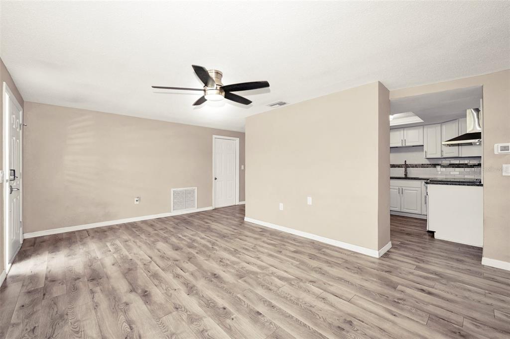 An empty living room with wood-look flooring, a ceiling fan, and an adjacent kitchen — 10910 BRIDLETON ROAD, PORT RICHEY, FL