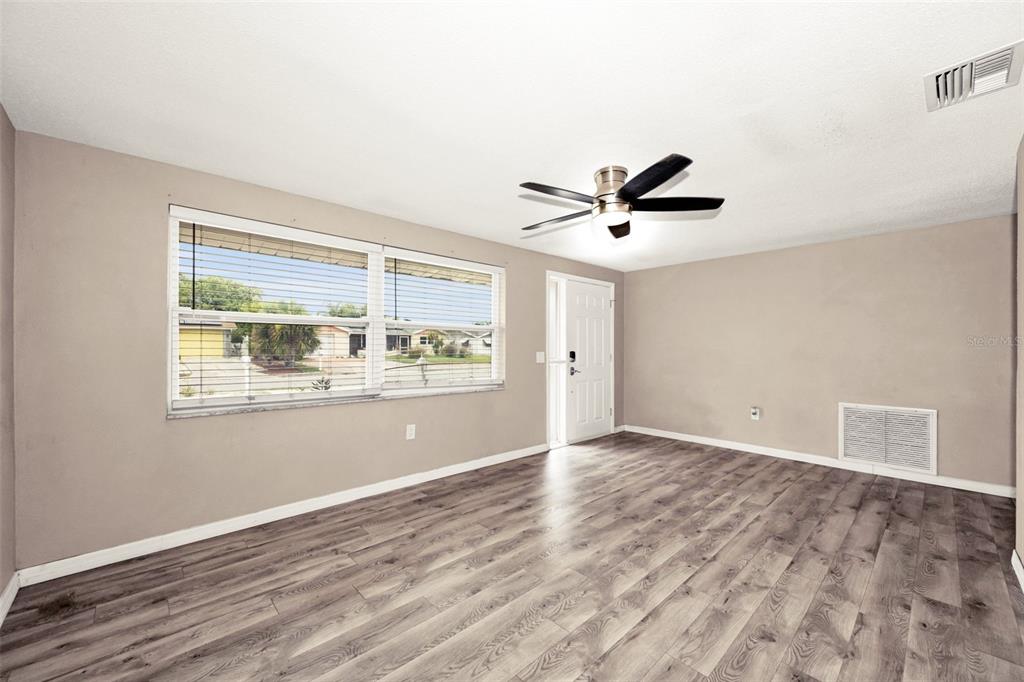 An empty room features light brown walls, wood-look flooring, a ceiling fan, and large windows — 10910 BRIDLETON ROAD, PORT RICHEY, FL