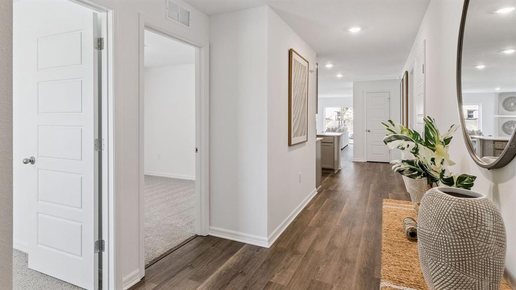 A hallway with wood-look flooring leads past a carpeted bedroom toward an open living area — 1731 GRANDIOSE DRIVE, HAINES CITY, FL