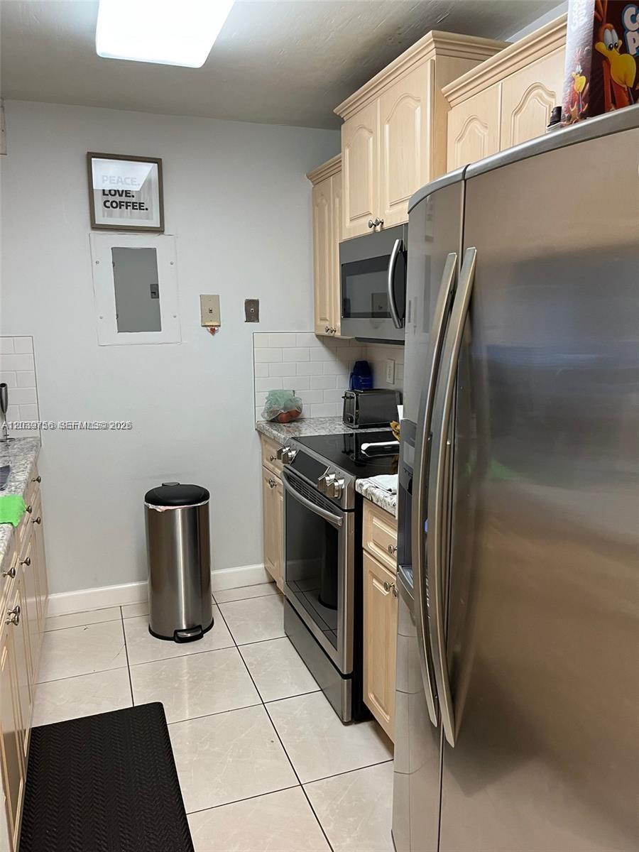 A galley-style kitchen features light wood cabinets, stainless steel appliances, and white tile flooring — 10135 NW 9th St Cir # 208, Miami FL 33172, MIAMI, FL