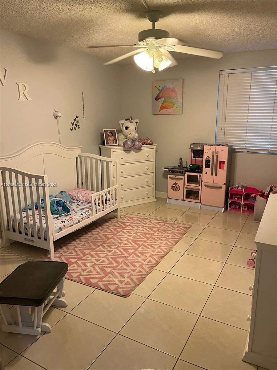 A child's bedroom features a white crib, a dresser, a toy kitchen, and a patterned rug — 10135 NW 9th St Cir # 208, Miami FL 33172, MIAMI, FL