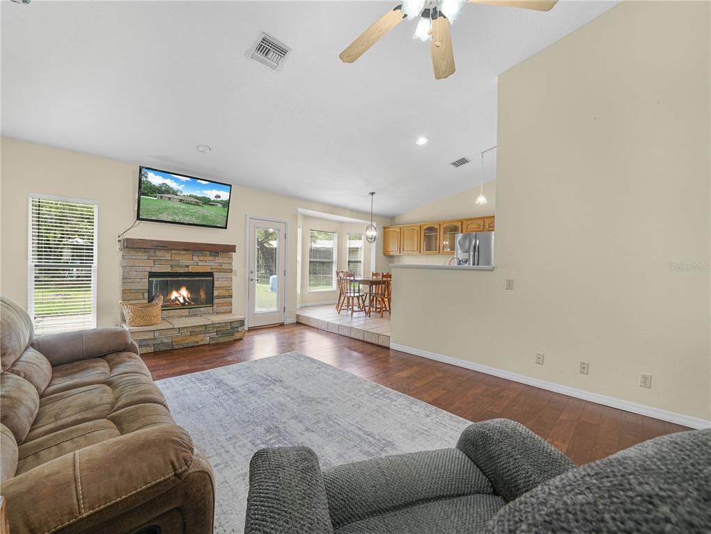 A living room with a stone fireplace, wood floors, and an adjacent dining area — 3437 MAR LISA COVE ROAD, LAKE WALES, FL