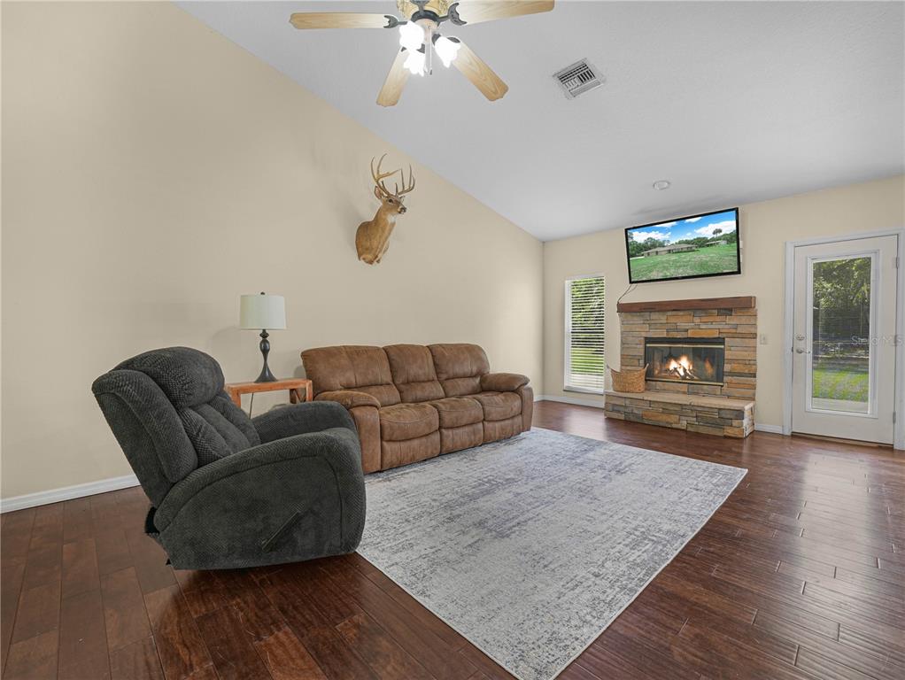 A living room features a stone fireplace, a brown sofa, a recliner, and wood flooring — 3437 MAR LISA COVE ROAD, LAKE WALES, FL