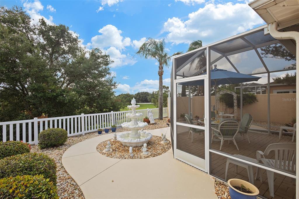 A backyard patio features a tiered fountain, a white fence, and a screened-in dining area — 867 OVIEDO ROAD, LADY LAKE, FL