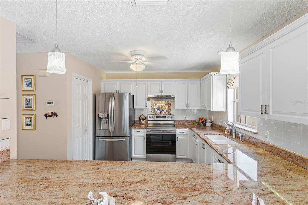A kitchen features white cabinets, granite countertops, stainless steel appliances, and two pendant lights — 867 OVIEDO ROAD, LADY LAKE, FL