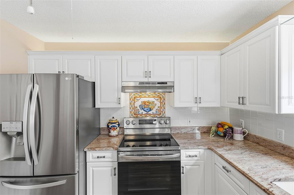 A kitchen features white cabinets, stainless steel appliances, and granite countertops with a tiled backsplash — 867 OVIEDO ROAD, LADY LAKE, FL