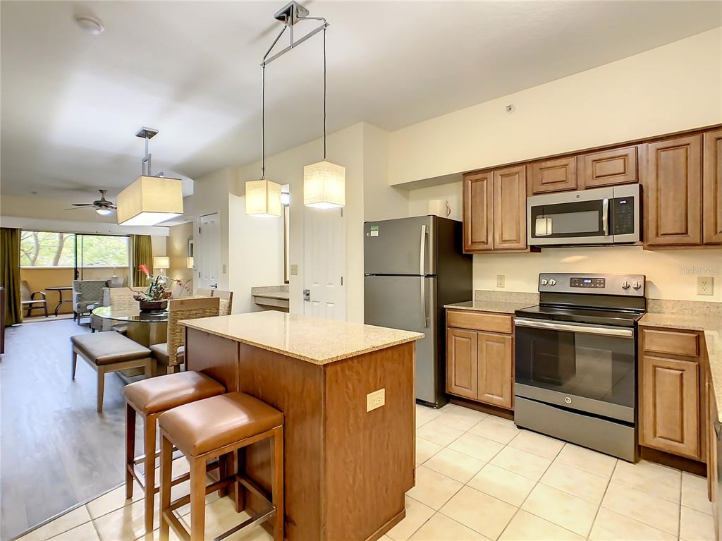 A kitchen with wood cabinets, stainless steel appliances, and a granite-topped island with bar stools — 12538 FLORIDAYS RESORT DR UNIT C-211, ORLANDO, FL