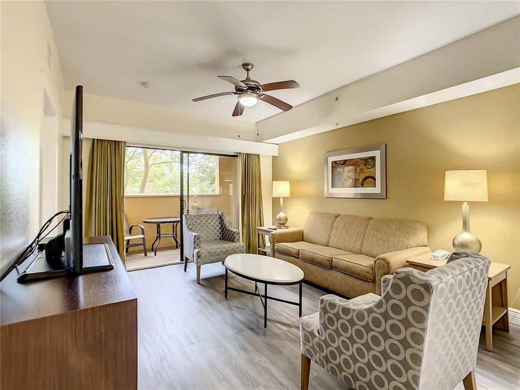A living room features a beige sofa, patterned armchairs, a coffee table, and a balcony view — 12538 FLORIDAYS RESORT DR UNIT C-211, ORLANDO, FL