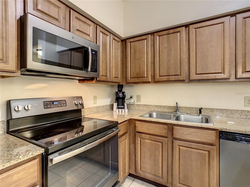 A kitchen features wood cabinets, stainless steel appliances, and granite countertops — 12538 FLORIDAYS RESORT DR UNIT C-211, ORLANDO, FL