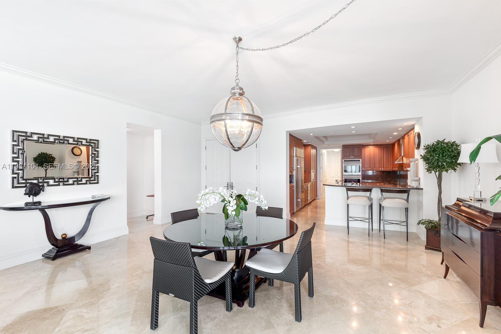 A dining area with a glass table, dark chairs, and a kitchen with wooden cabinets — 10295 Collins Ave # 803, Bal Harbour FL 33154, BAL HARBOUR, FL