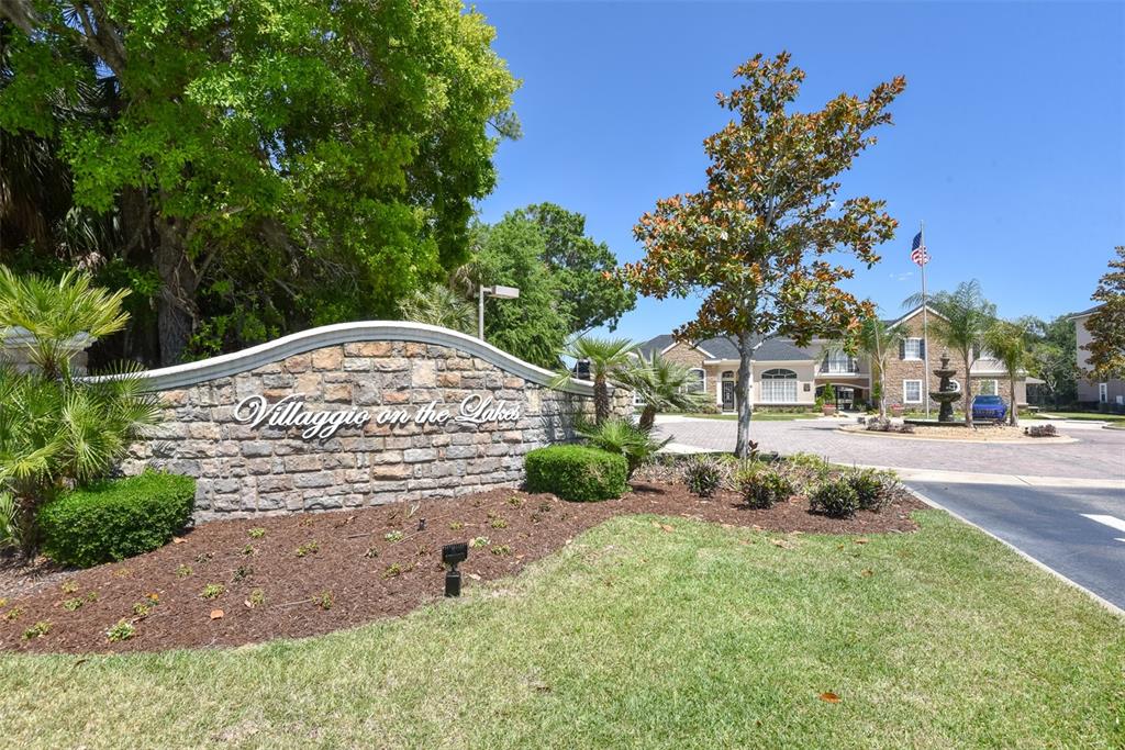 A two-story building with stone siding, a dark shingled roof, and a paved parking area — 940 VILLAGE TRAIL UNIT 6-103, PORT ORANGE, FL