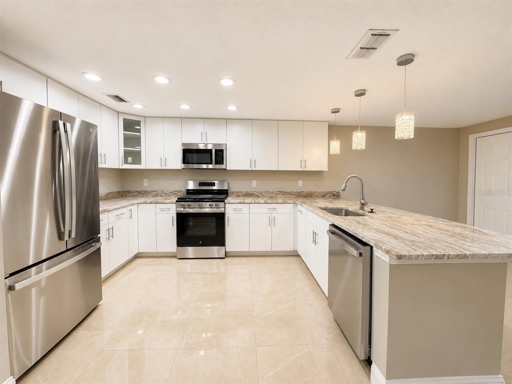 A kitchen with white cabinets, stainless steel appliances, and a stone countertop island — 5419 DENVER STREET NE, ST PETERSBURG, FL