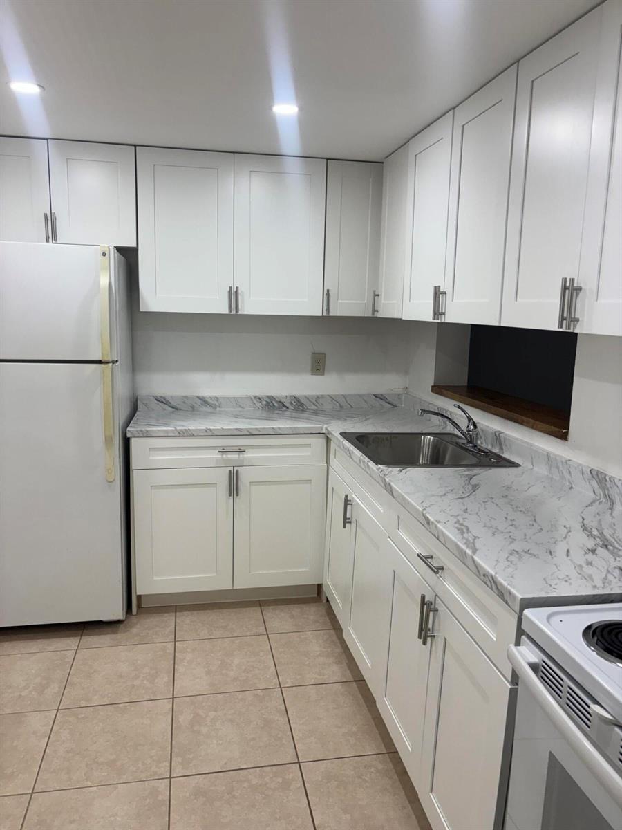 A kitchen features white shaker cabinets, marble-patterned countertops, a stainless steel sink, and tile flooring — 5190 Las Verdes Circle # 315, Delray Beach FL 33484, DELRAY BEACH, FL