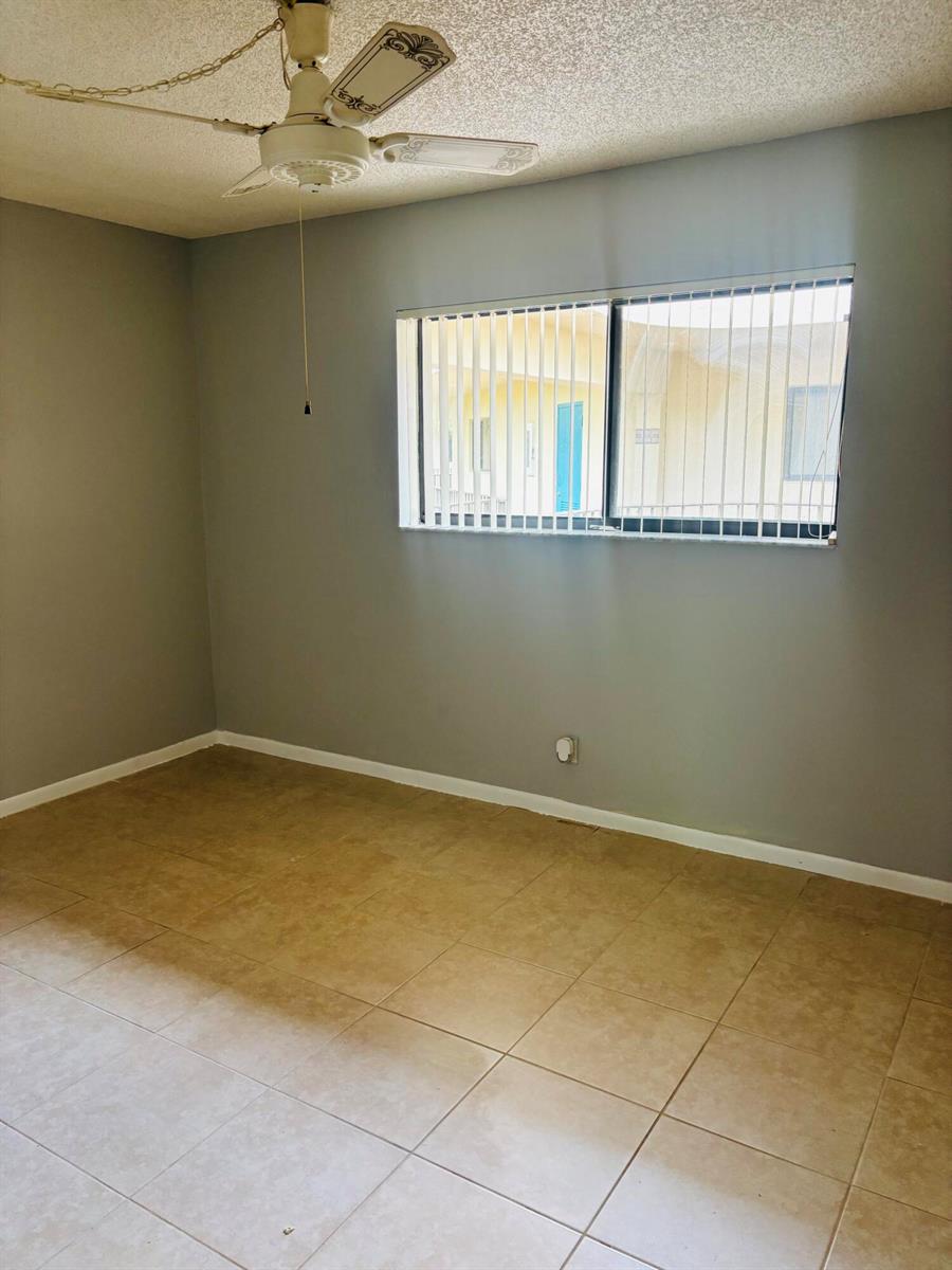 An empty room features gray walls, beige tile flooring, a ceiling fan, and vertical blinds — 5190 Las Verdes Circle # 315, Delray Beach FL 33484, DELRAY BEACH, FL