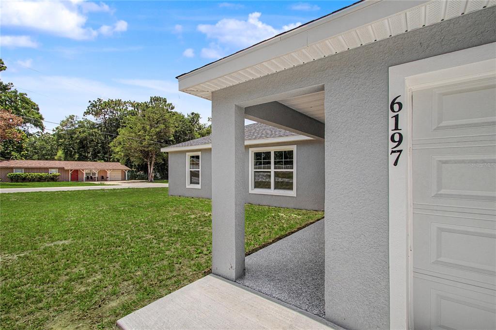 A gray stucco house exterior features a covered entryway, a garage door, and a lawn — 6197 NW 61ST STREET, OCALA, FL