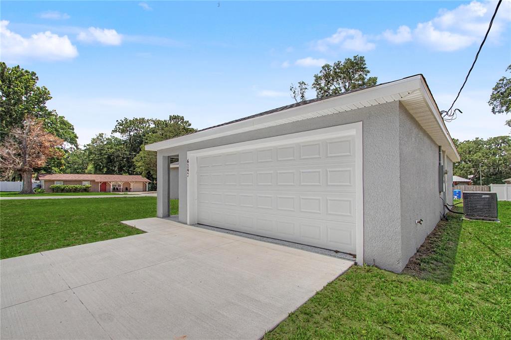 A detached gray stucco garage with a white sectional door and a concrete driveway — 6197 NW 61ST STREET, OCALA, FL