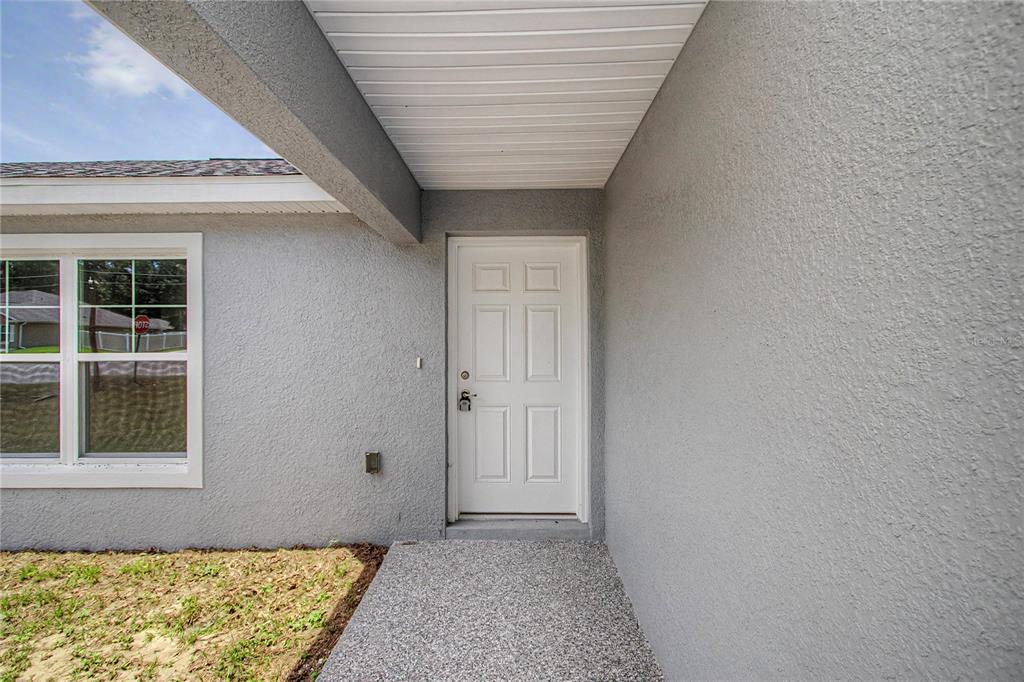 A white front door is centered on the gray stucco exterior wall of a house — 6197 NW 61ST STREET, OCALA, FL