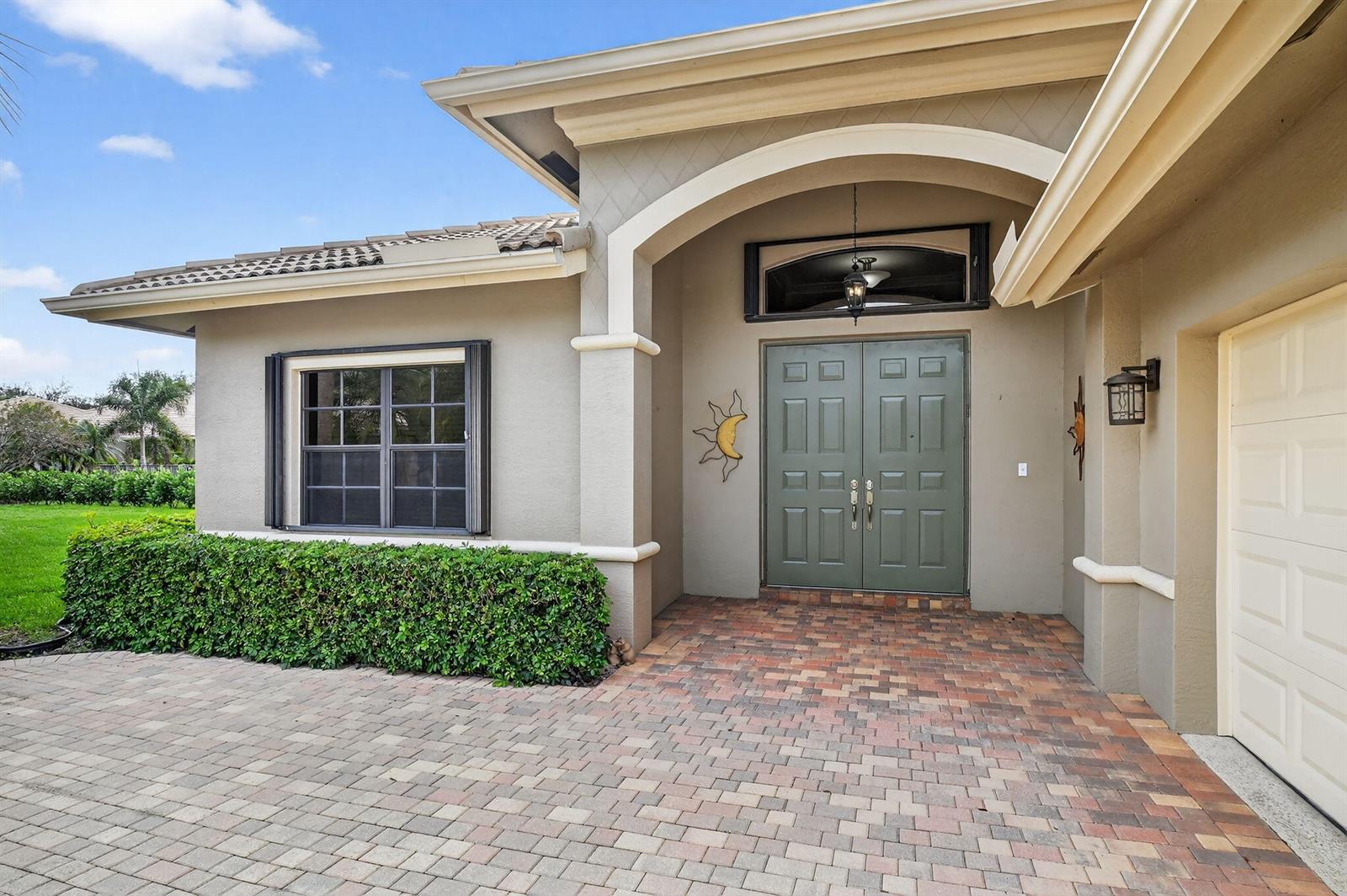 A beige house exterior features a brick paver driveway, double green doors, and a hedge — 8046 Via Grande, Boynton Beach FL 33437, BOYNTON BEACH, FL