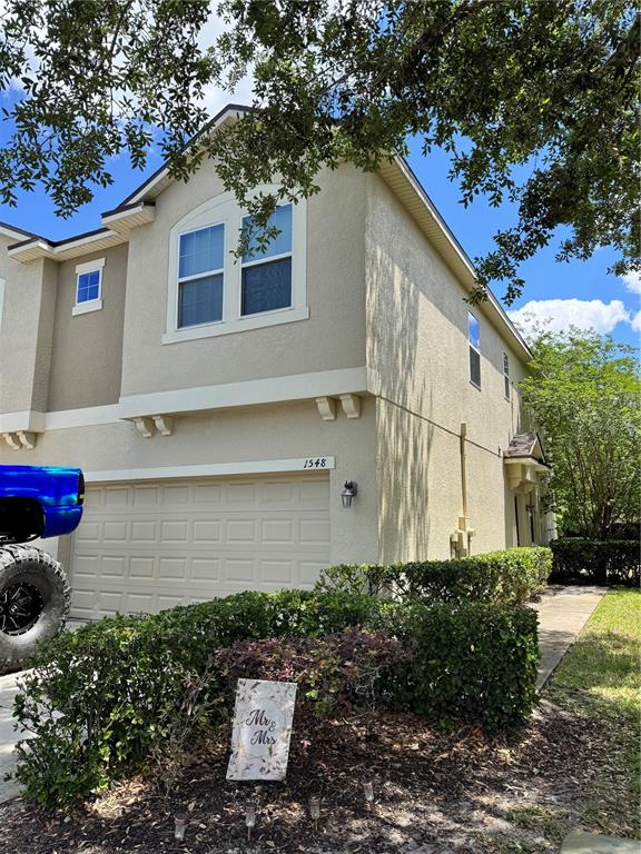 A two-story tan stucco townhouse features a garage, a driveway, and a landscaped front yard — 1548 PURPLE PLUM LANE, OVIEDO, FL