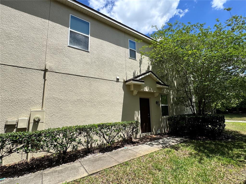 A beige stucco townhouse exterior features a dark front door, a sidewalk, and landscaping — 1548 PURPLE PLUM LANE, OVIEDO, FL