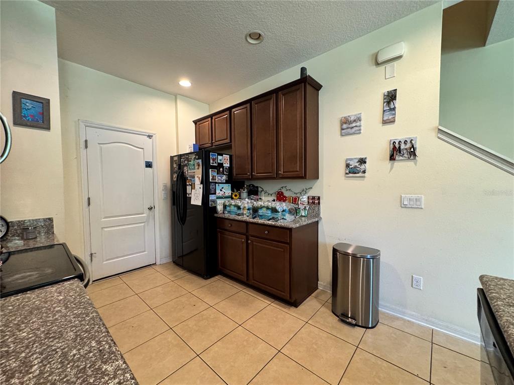 A kitchen features dark wood cabinets, a black refrigerator, and tan tile flooring — 1548 PURPLE PLUM LANE, OVIEDO, FL