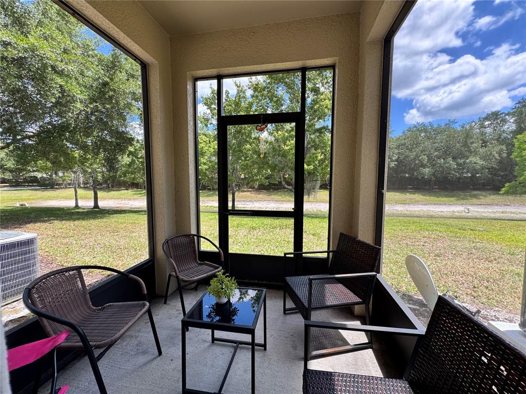 A screened-in porch features a small table, four chairs, and views of a grassy yard — 1548 PURPLE PLUM LANE, OVIEDO, FL