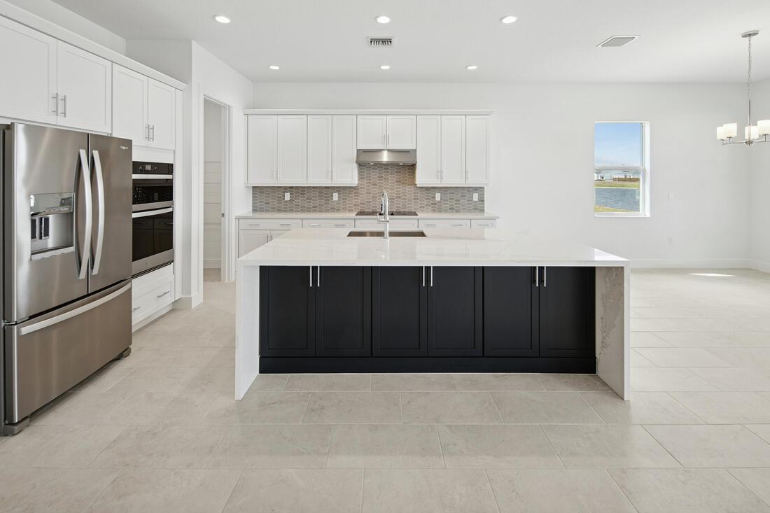 A modern kitchen features white cabinetry, a dark island, stainless steel appliances, and tile flooring — 2810 68th Street, Vero Beach FL 32967, VERO BEACH, FL