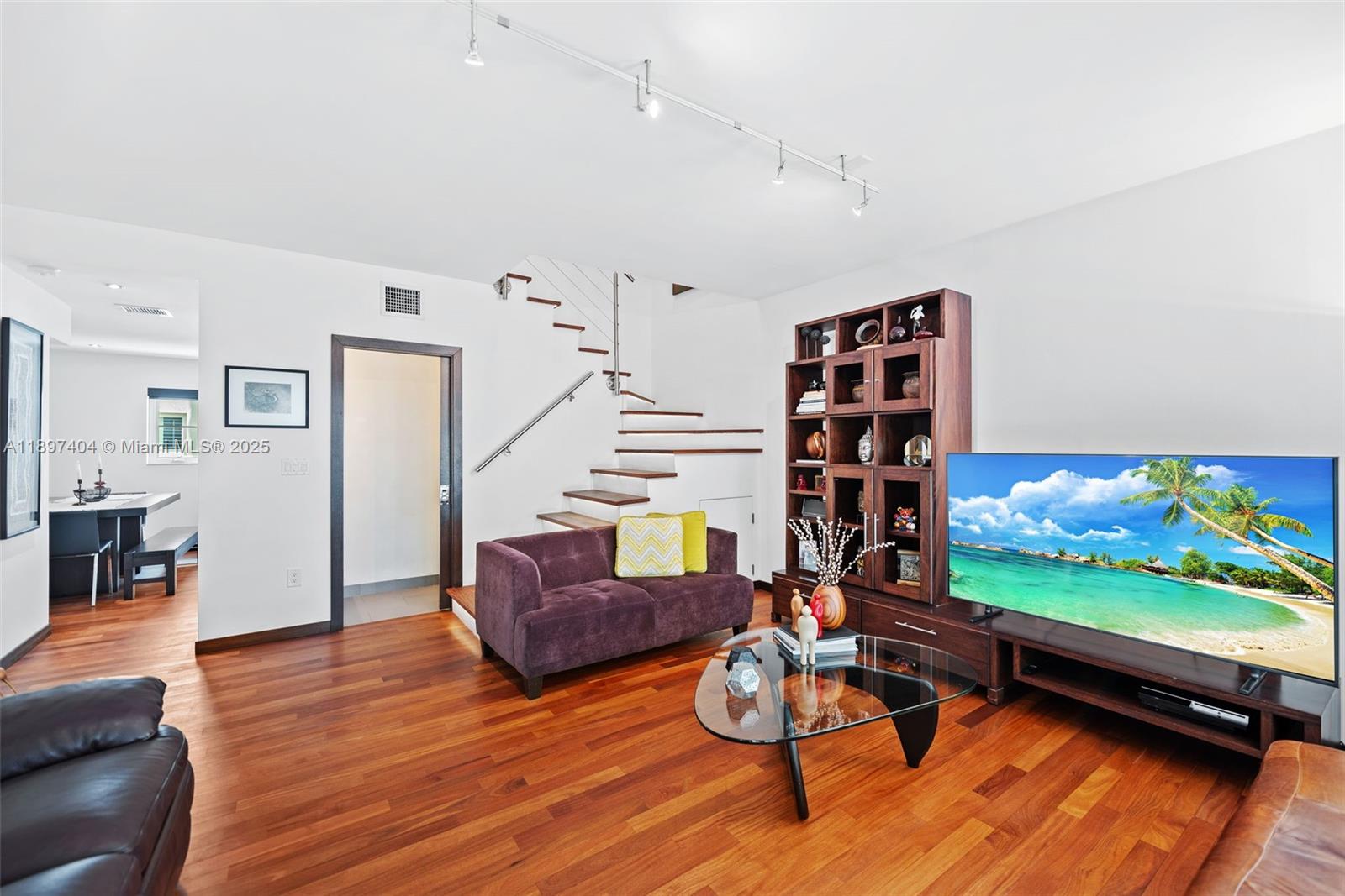 A living room features a purple sofa, a glass coffee table, and a wooden staircase — 261 Navarre Ave # 3, Coral Gables FL 33134, CORAL GABLES, FL