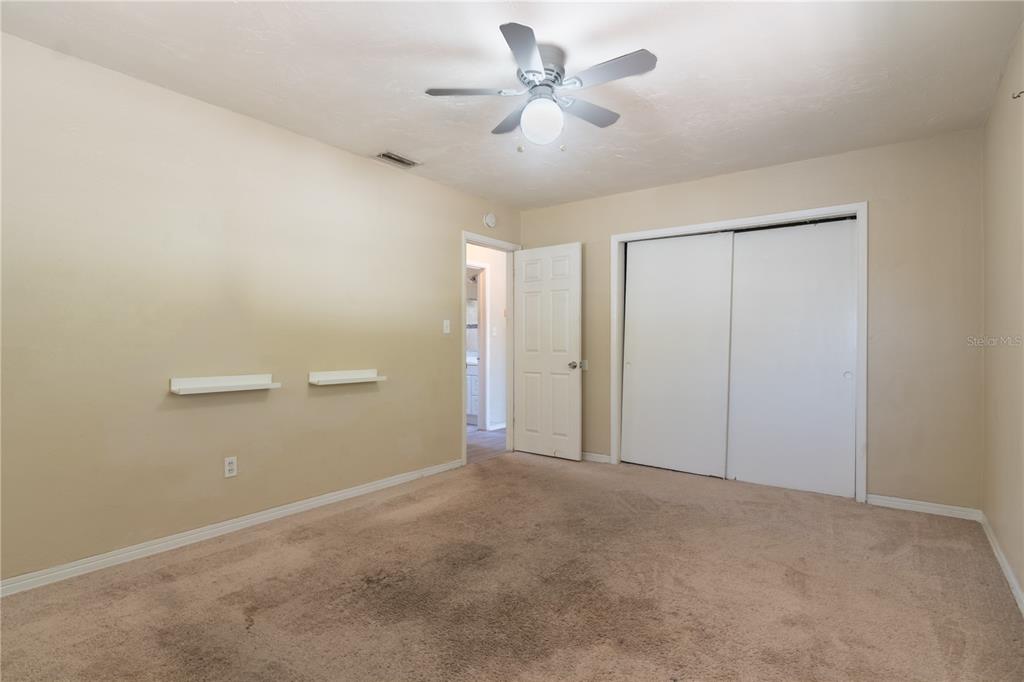A bedroom with beige walls, tan carpeting, a ceiling fan, and sliding closet doors — 1415 WOOD AVENUE, CLEARWATER, FL