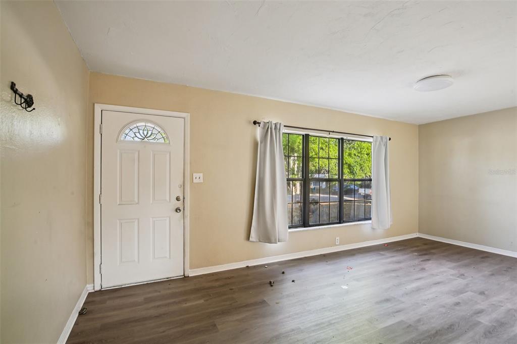 An empty room features light tan walls, dark wood-look flooring, a white door, and windows — 1415 WOOD AVENUE, CLEARWATER, FL