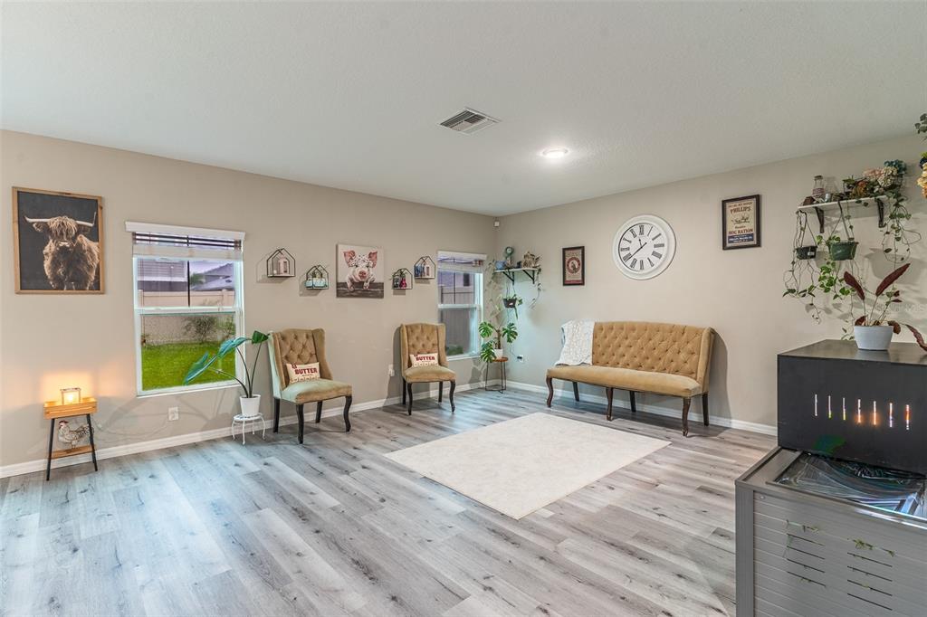 A living room features light wood-look flooring, two windows, a tufted bench, and farmhouse-style decor — 5508 ARLINGTON RIVER DRIVE, LAKELAND, FL
